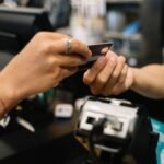 Mão segurando passaporte e cartões de crédito internacionais, representando o uso do cartão em viagens ao exterior