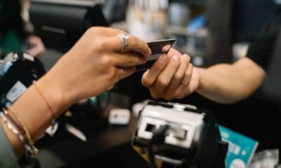Mão segurando passaporte e cartões de crédito internacionais, representando o uso do cartão em viagens ao exterior